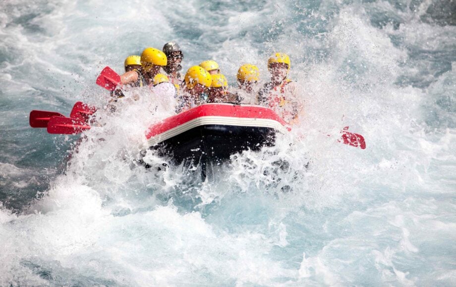 People with yellow helmets in raft going through rapids