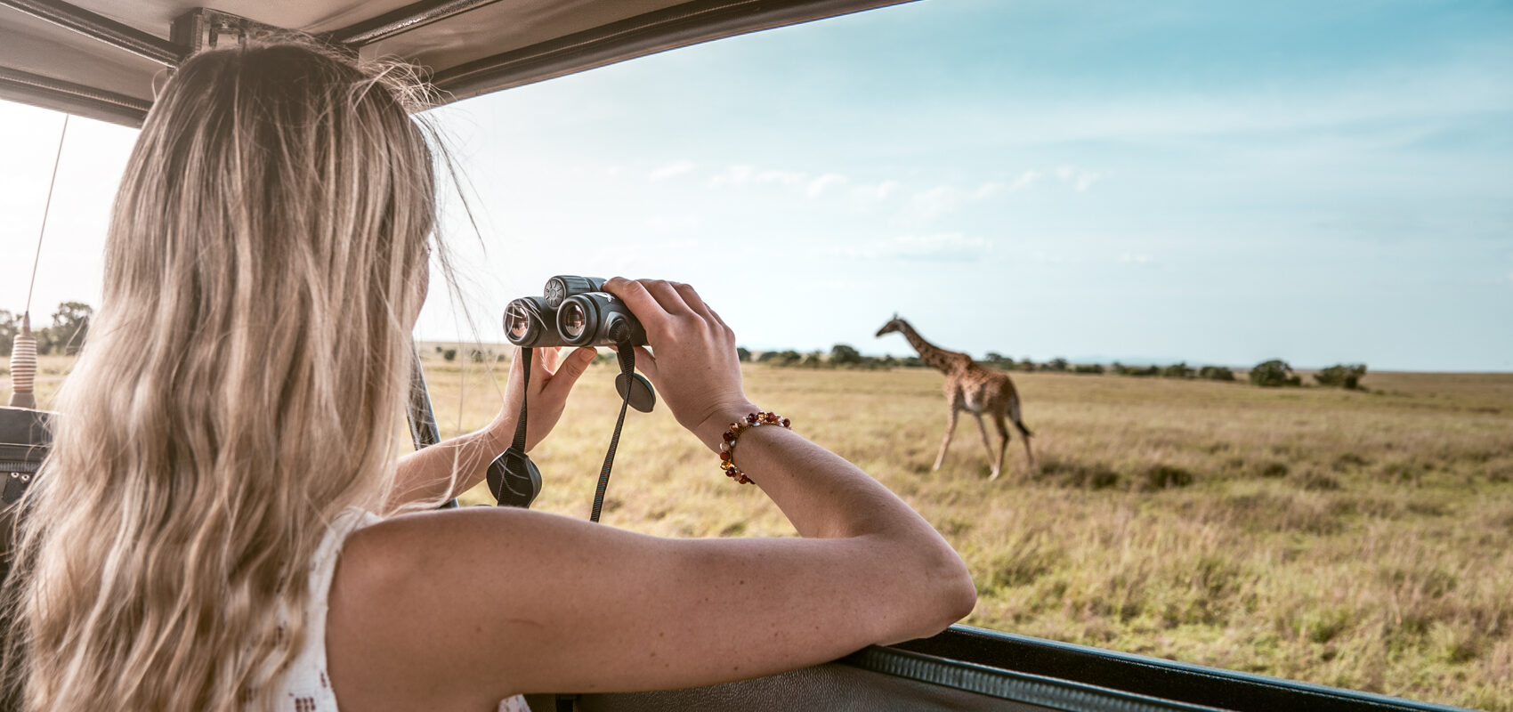 Kvinde i safarijeep med kikkert kigger på giraffer