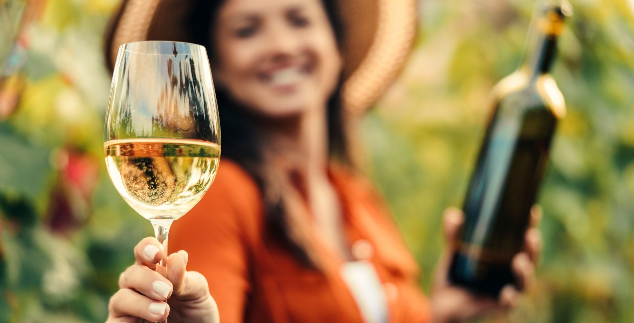 En glad kvinde skåler i et glas sydafrikansk hvidvin og holder en vinflaske i den anden hånd