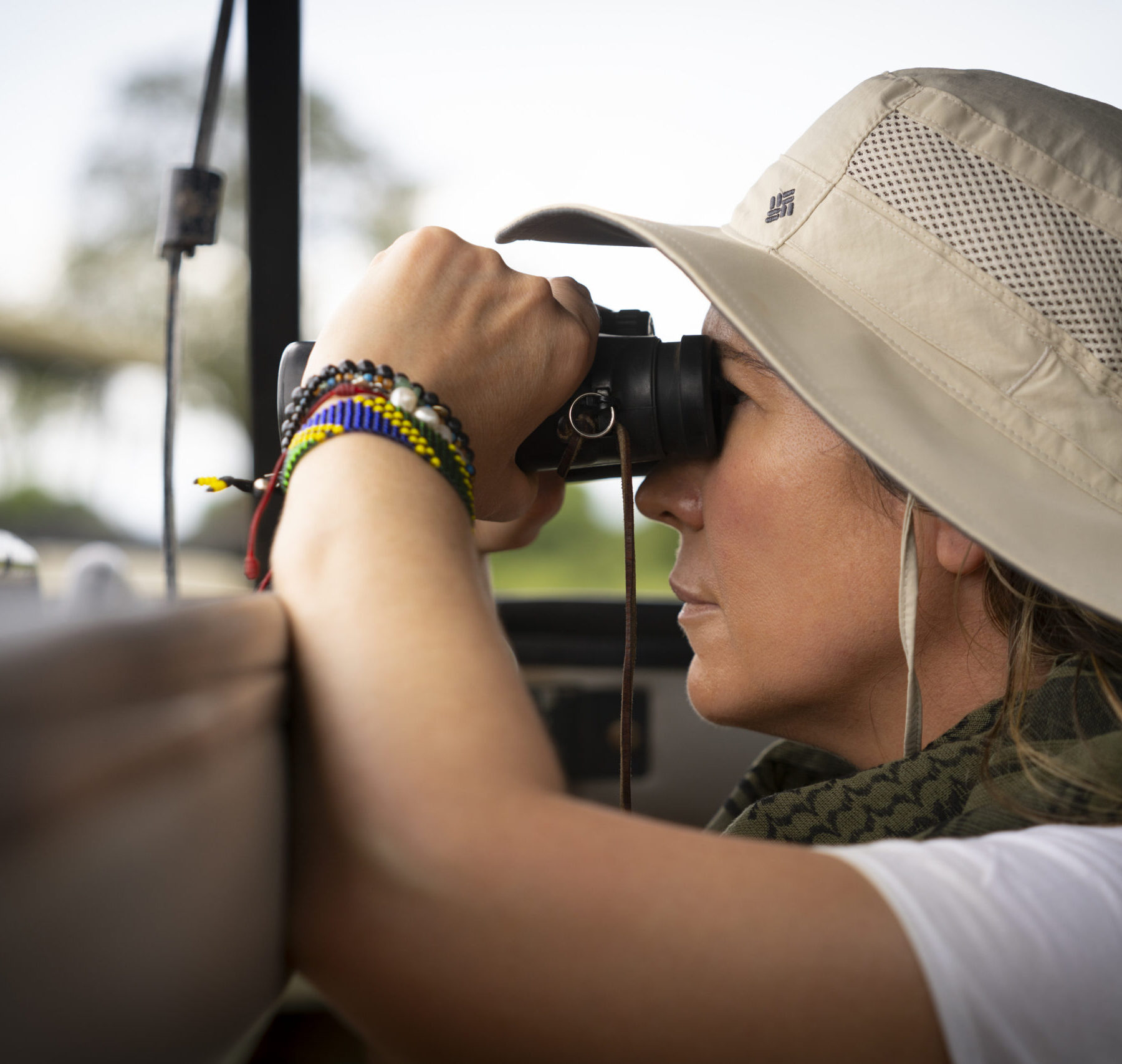 Kvinde med hat og kikkert kigger ud fra en safari-jeep.