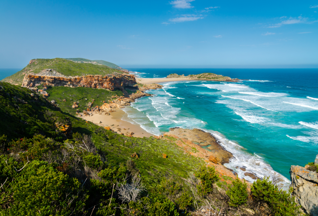 Naturskønt kystlandskab med barske klipper, sandstrand og turkisblåt hav i Sydafrika
